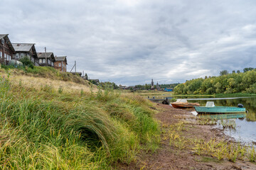 Boats on the river bank against the backdrop of log houses and an old wooden church.