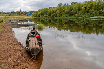 Boats on the river bank against the backdrop of log houses and an old wooden church.