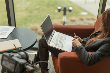 A woman is comfortably sitting in a chair while actively using a laptop computer to perform tasks...