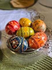 A vibrant display of meticulously decorated Easter eggs, known as pysanky, rests on a glass plate,...