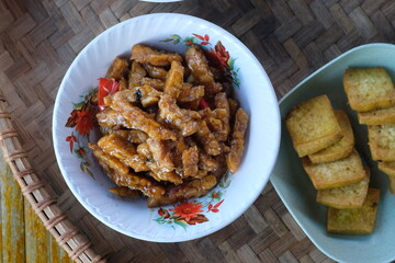 orek tempe or oseng tempe. made from tempeh, sliced garlic, shallots, chili, soy sauce. Indonesian food. served in a white bowl