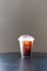 Iced americano coffee in a disposable glass on table. Cold summer drink on grey background with copy space.
