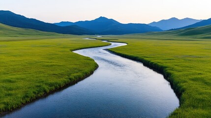 A winding river flows through lush green meadows with distant mountains under a clear sky.