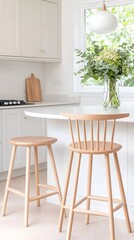 Bright kitchen with light wood stools, a curved counter, and a vase of greenery near a window