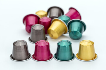Colorful coffee capsules scattered on white background, featuring vibrant hues of pink, gold, teal, and silver. arrangement creates lively and inviting atmosphere