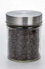 Glass jar filled with roasted coffee beans is sealed with metal lid, showcasing rich texture and dark color of beans. jar is placed against plain background, highlighting its contents