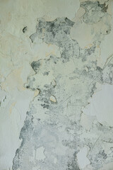 A wall with peeling white paint reveals darker patches underneath, showing age and damage.