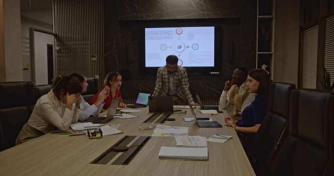 Diverse people in a late-night office meeting struggle with a challenging project. Exhaustion and frustration are evident as they grapple with the task at hand.
