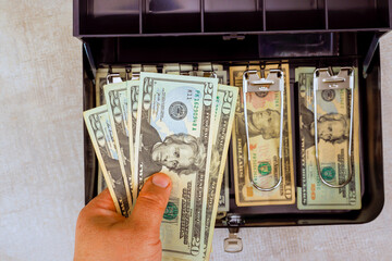 Fototapeta na wymiar Hand with American dollars banknotes shows money management in cash box filled with various denominations.