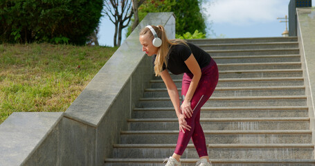 Exhausted woman resting on stairs after intense jogging workout outdoors.