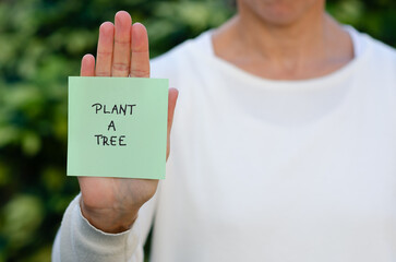 A woman holding a green handwritten sign reminder of planting a tree.