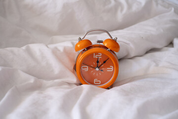 Orange alarm clock on white bed. Fashionable minimalist style. Time, business and technology...