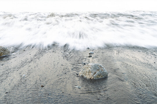 Ocean Wave Blurring Over Rock on Sandy Beach