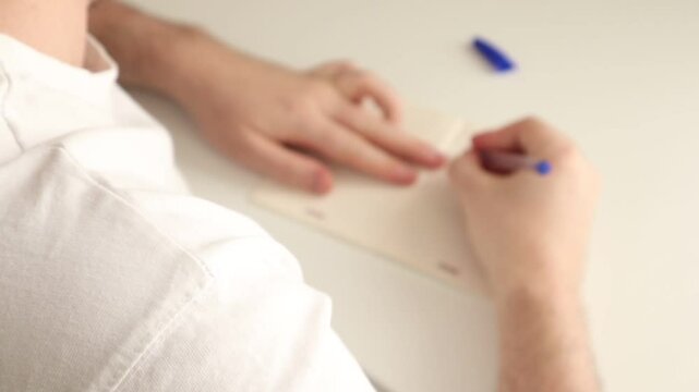 A man makes edits to his to-do list in his medium-sized notebook with a pen