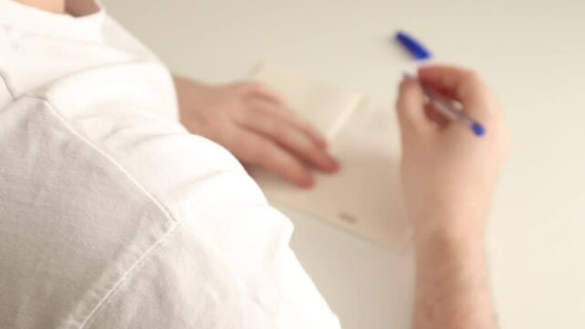 A man kneads his back after a long session of writing a script with a pen in a notebook