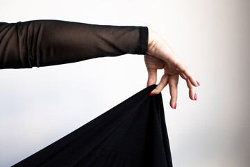 Female hand draping black fabric with red nails and sheer sleeve