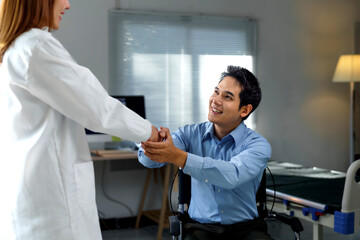 Doctor shaking hands with a smiling patient in a wheelchair, showing support and empathy in a...