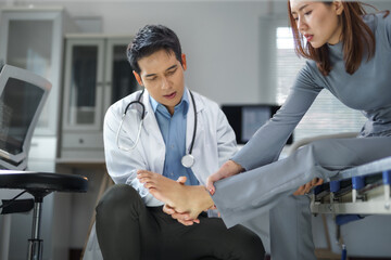 Asian doctor examining injured foot of businesswoman sitting on examination table in hospital room