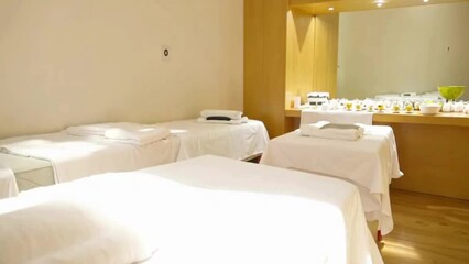 Soft sunlight illuminating pristine white massage table, crisp folded towels, tranquil wellness salon interior preparing for relaxing body treatment