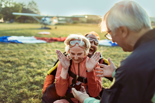 Senior man proposing after skydiving as woman reacts with joy on landing field