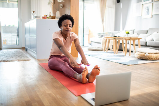 Woman stretching on yoga mat during online home workout session
