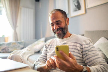 Happy man reading a message on smartphone while relaxing at home