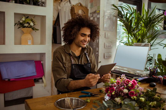 Young male florist using digital tablet at flower shop counter - Powered by Adobe