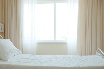 Fototapeta premium Empty bed in a medical setting near a bright window with white curtains, signaling patient care and clinical environment. Symbolizes recovery or rest.