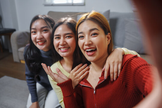 Three young women are smiling and taking a selfie together in their living room, enjoying their friendship and creating memories - Powered by Adobe