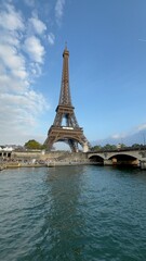 Obraz premium Iconic view of the Eiffel Tower from the Seine River on a sunny day with clear blue skies. A classic Parisian scene capturing architecture, water, and tourism.
