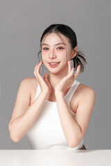 Naklejka premium Happy young woman smiling with hands on face against gray background