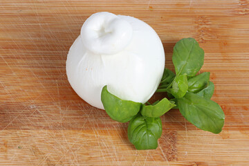 A closed ball of burrata cheese on a wooden cutting board with fresh basil leaves, rustic and fresh presentation