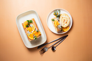 Orange sponge roll with cream and mint in a white plate on a bright background