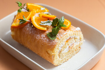 Orange sponge roll with cream and mint in a white plate on a bright background