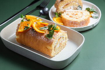 Orange sponge roll with cream and mint in a white plate on a bright background
