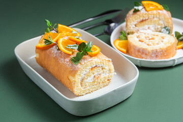 Orange sponge roll with cream and mint in a white plate on a bright background