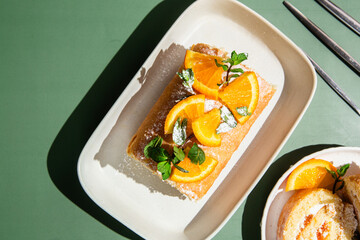 Orange sponge roll with cream and mint in a white plate on a bright background