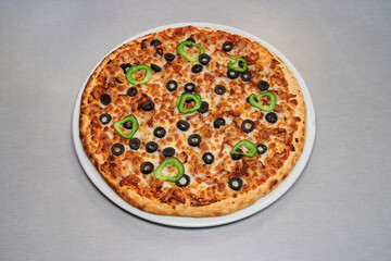 A pizza with olives and peppers on it. The pizza is on a white plate. The plate is on a table