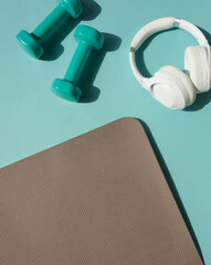 Sport or workout concept flat lay with blue dumbbells, sneakers, and yoga mat on the blue teal...
