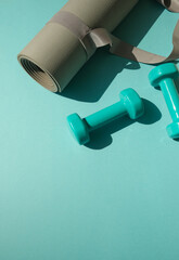 Sport or workout concept flat lay with blue dumbbells and yoga mat on the blue teal background. Copy space