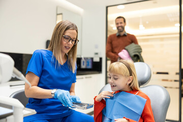 Obraz premium The smiling girl enjoys her dental visit as the professional dentist engages positively with her, ensuring a reassuring atmosphere.
