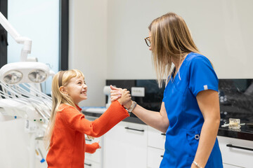 Fototapeta premium A young girl and her dentist share a joyful moment after the dental appointment, highlighting their positive and trusting relationship.