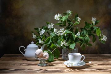 A cup of tea, a white teapot, a sugar bowl, homemade marshmallows and a bouquet of jasmine on a wooden table
