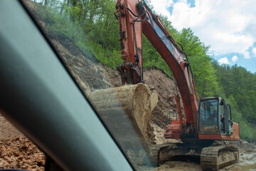 Construction site with a large excavator in action, seen from a car window. Captures infrastructure...