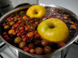 A compote of fresh apples and a mix of berries is brewed in a saucepan with water. Apples berries simmering, top view