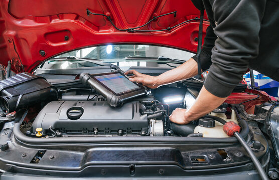 Mechanic diagnosing car engine problems using digital tablet in auto repair shop