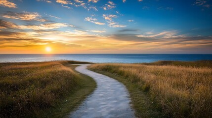 Winding path through golden marsh grass leads to sunset over ocean horizon beneath dramatic cloudy sky