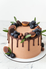 Chocolate cake decorated with blueberries, cookies and candies on a white background. Brown cream cheese frosting with dark chocolate drips on birthday cake