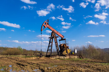 Old Oil Pump Jack Operating in Rural Field.Working oil well pump on muddy terrain.Fossil Fuel...