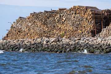 Massive Timber Storage by the Sea with Rocky Shore and Industrial Stacked Logs under Blue Sky..